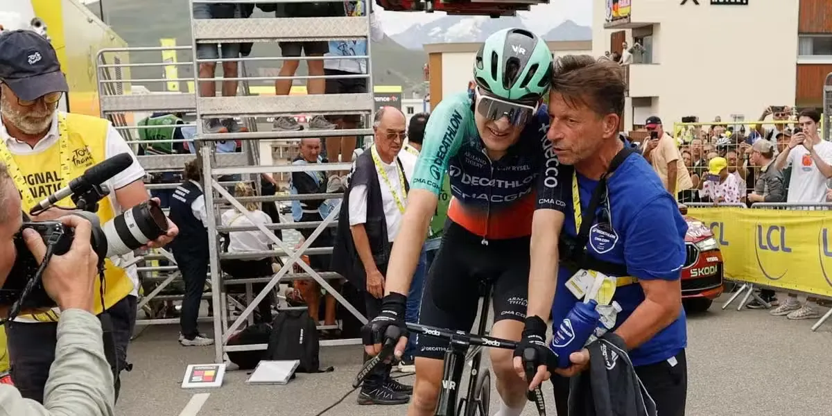 Paul Seixas, soutenu par son assistant et masseur, Sabino Pignatelli, à l’arrivée à l’Alpe d’Huez